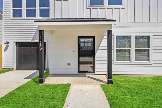 doorway to property featuring an attached garage, board and batten siding, concrete driveway, and a yard