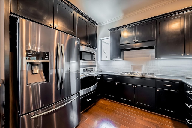 kitchen with dark wood finished floors, appliances with stainless steel finishes, crown molding, dark cabinets, and backsplash