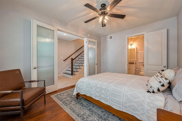 bedroom featuring a ceiling fan, wood finished floors, visible vents, baseboards, and ensuite bath