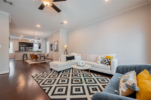 living room with visible vents, dark wood-type flooring, ornamental molding, baseboards, and ceiling fan