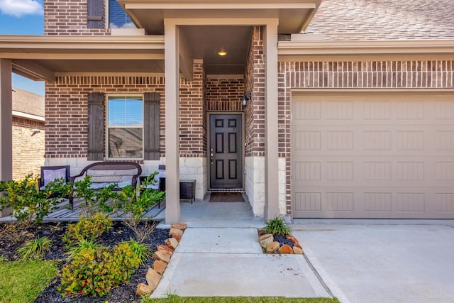 view of exterior entry featuring brick siding, an attached garage, covered porch, and driveway