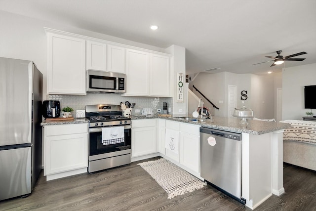 kitchen featuring open floor plan, stainless steel appliances, a peninsula, white cabinets, and dark wood-style flooring