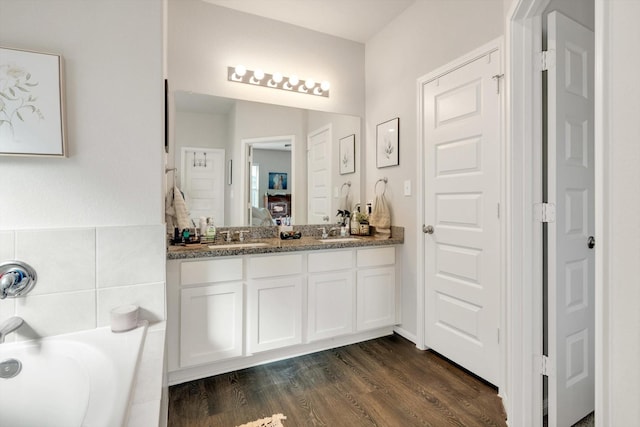 ensuite bathroom with a sink, wood finished floors, ensuite bath, double vanity, and a bath