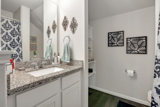 bathroom with vanity, toilet, wood finished floors, and baseboards