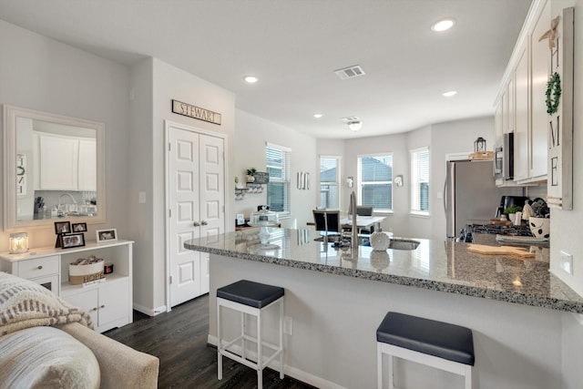 kitchen featuring light stone counters, stainless steel appliances, a peninsula, and white cabinets