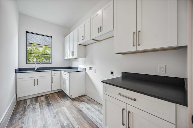 kitchen featuring white cabinetry, dark countertops, light wood-type flooring, and a sink