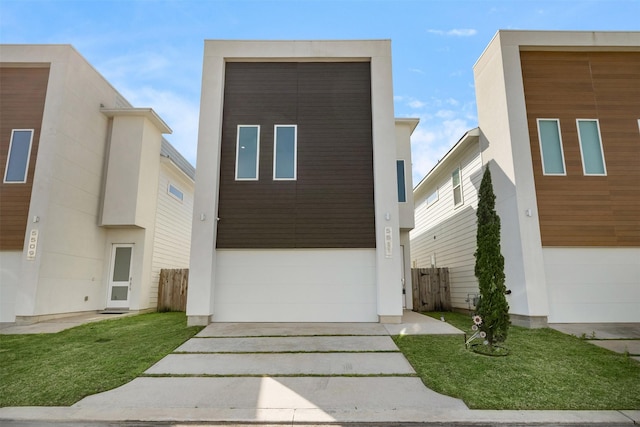 modern home featuring an attached garage, concrete driveway, a front yard, and fence