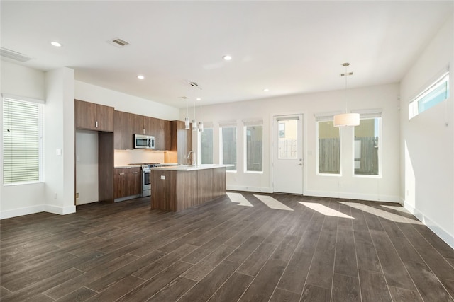 kitchen with a center island with sink, dark wood finished floors, recessed lighting, light countertops, and appliances with stainless steel finishes