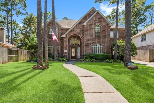 view of front of house featuring brick siding, roof with shingles, a front lawn, and fence