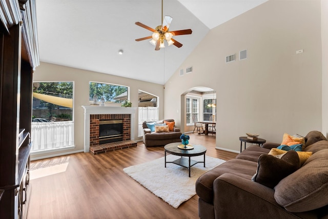 living room with visible vents, a brick fireplace, ceiling fan, wood finished floors, and arched walkways