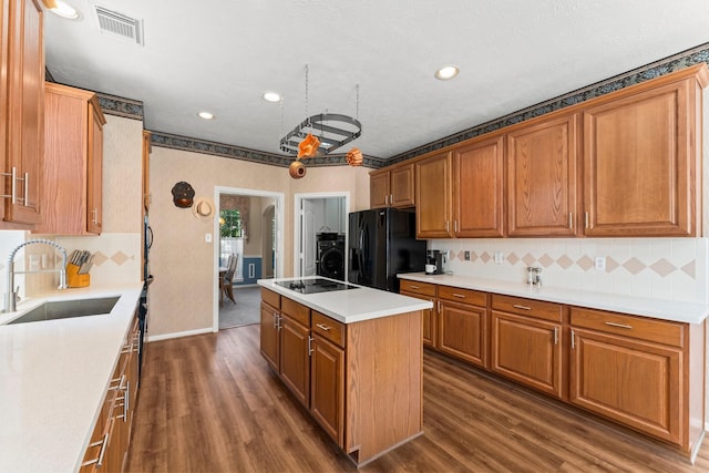 kitchen featuring visible vents, a center island with sink, washer / clothes dryer, a sink, and black appliances