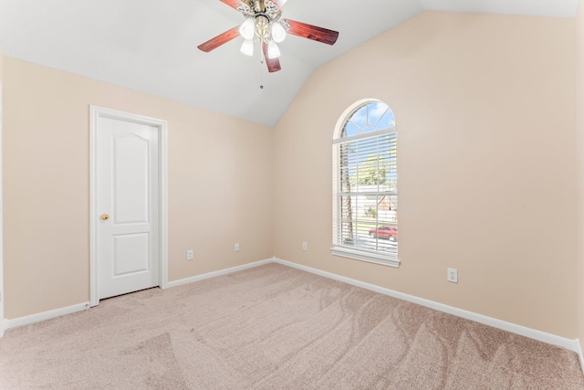 carpeted spare room with vaulted ceiling, a ceiling fan, and baseboards