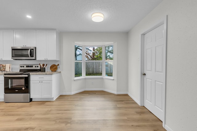 kitchen with white cabinets, light wood finished floors, baseboards, and appliances with stainless steel finishes