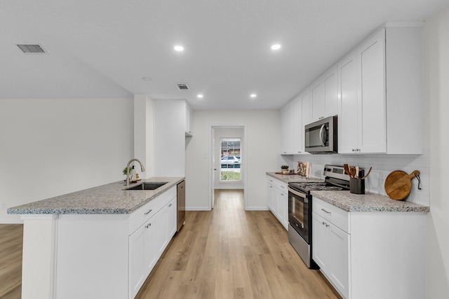 kitchen featuring visible vents, a sink, light wood-style floors, appliances with stainless steel finishes, and backsplash