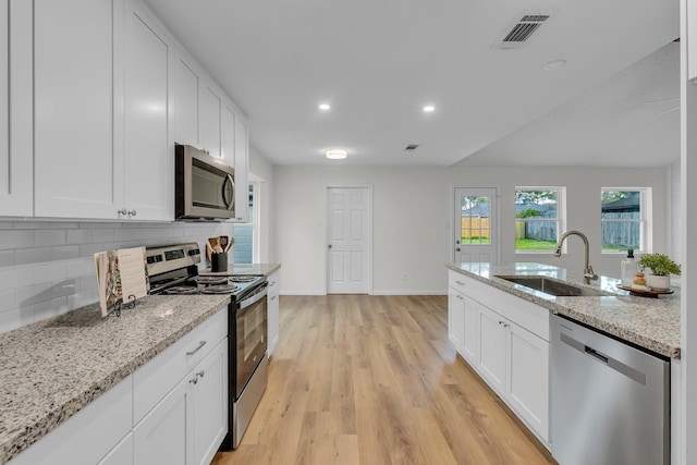 kitchen with visible vents, light wood-style flooring, a sink, decorative backsplash, and appliances with stainless steel finishes