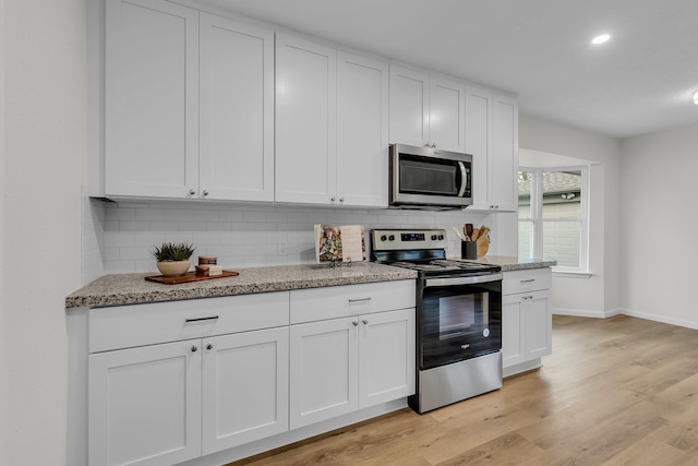 kitchen featuring light wood-type flooring, backsplash, white cabinetry, stainless steel appliances, and light stone countertops