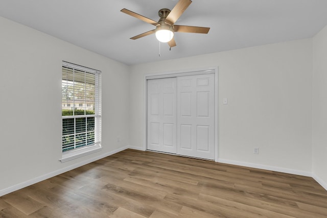 unfurnished bedroom featuring ceiling fan, a closet, baseboards, and wood finished floors