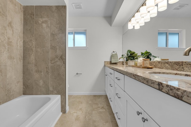 bathroom with double vanity, visible vents, a tub to relax in, and a sink