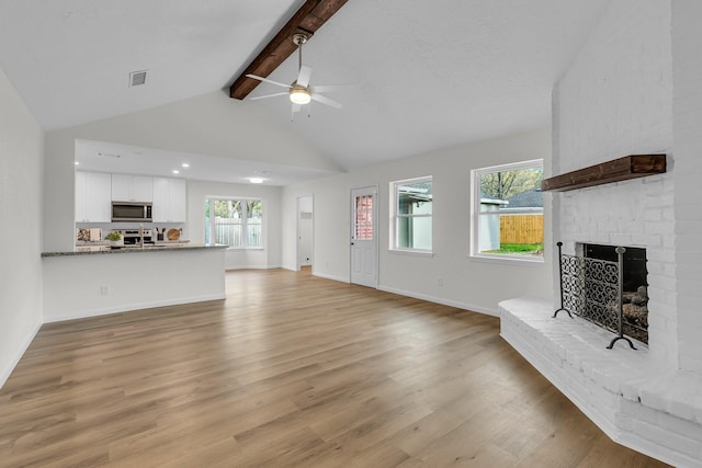 unfurnished living room featuring visible vents, beam ceiling, light wood-style flooring, a brick fireplace, and ceiling fan