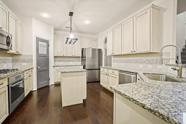 kitchen with hanging light fixtures, light stone counters, dark wood-style floors, stainless steel appliances, and a sink