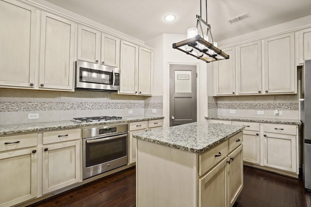 kitchen with visible vents, a kitchen island, dark wood finished floors, decorative backsplash, and appliances with stainless steel finishes