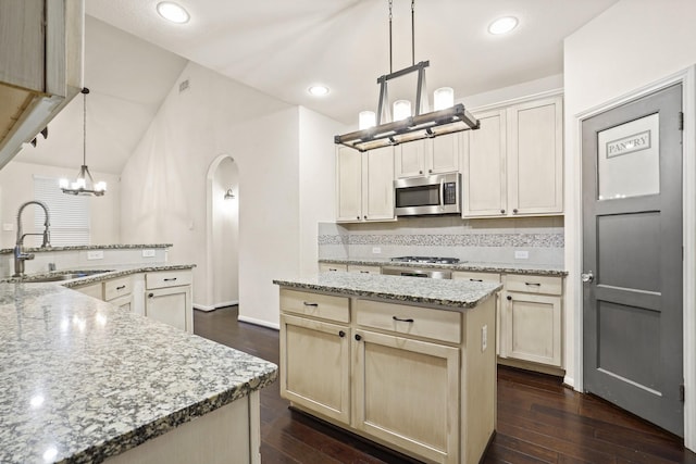 kitchen featuring arched walkways, a sink, decorative backsplash, appliances with stainless steel finishes, and a center island