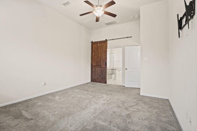 carpeted empty room with visible vents, a barn door, baseboards, and ceiling fan