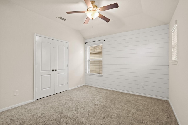 unfurnished bedroom with visible vents, a ceiling fan, carpet, wood walls, and vaulted ceiling