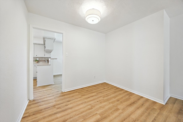 empty room featuring light wood-type flooring, baseboards, and a textured ceiling