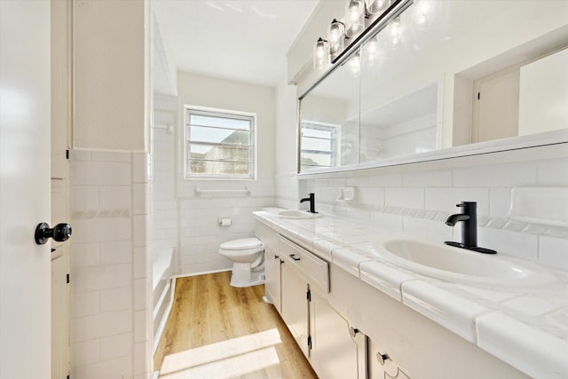 full bathroom featuring toilet, a sink, wood finished floors, tile walls, and double vanity