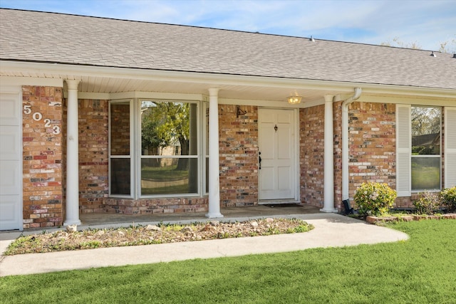 doorway to property with brick siding, covered porch, and a shingled roof