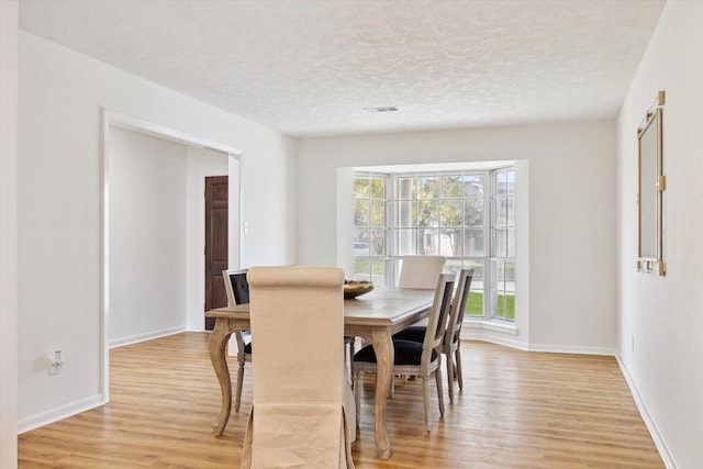 dining area featuring visible vents, baseboards, a textured ceiling, and light wood finished floors