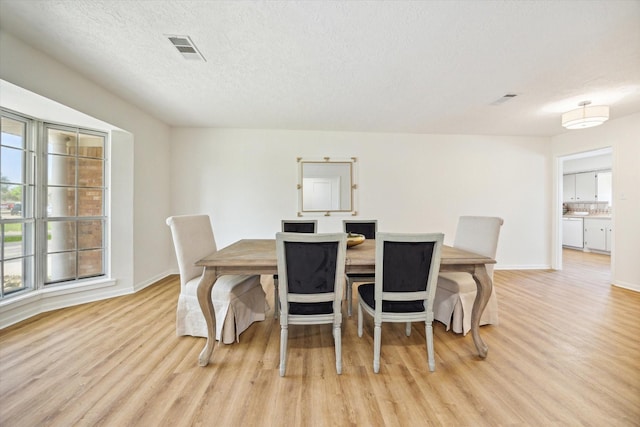 dining space with visible vents, a textured ceiling, and light wood-type flooring