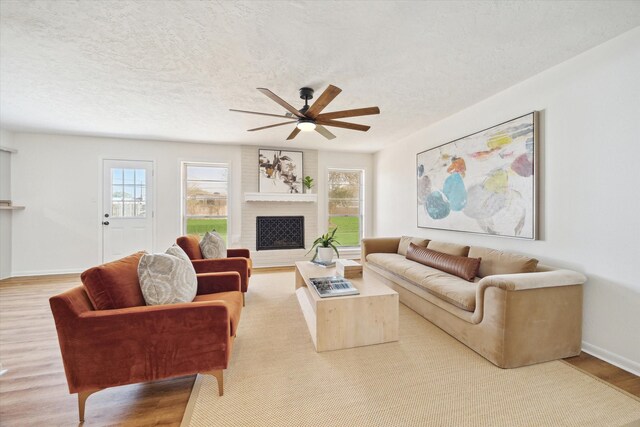 living room with wood finished floors, a ceiling fan, baseboards, a textured ceiling, and a brick fireplace