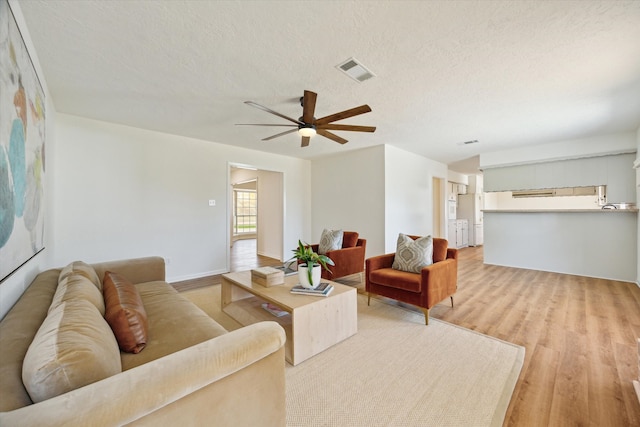 living area featuring light wood finished floors, visible vents, a textured ceiling, and a ceiling fan