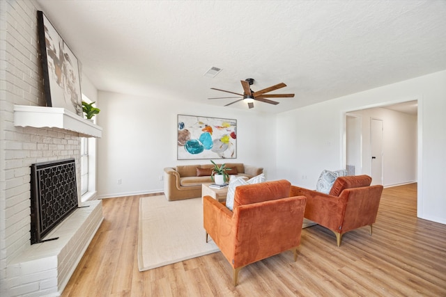 living room with visible vents, light wood-style floors, a fireplace, and a ceiling fan