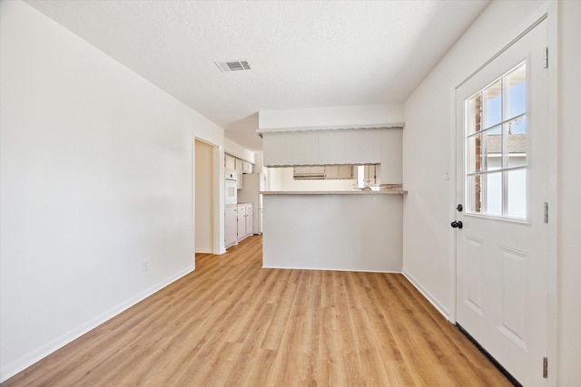 interior space featuring visible vents, baseboards, a textured ceiling, and light wood finished floors