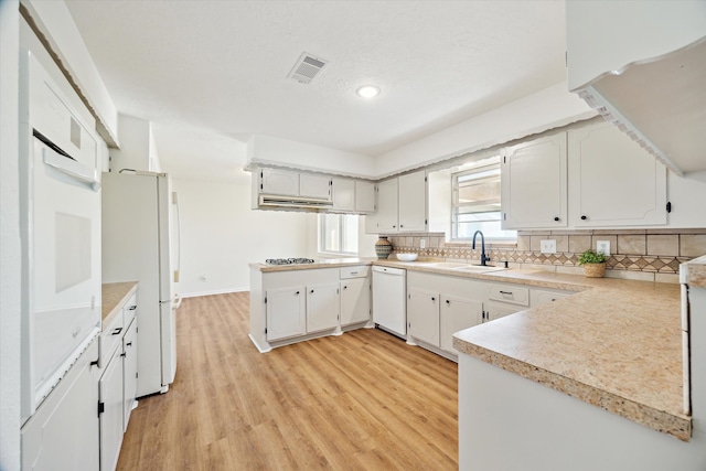 kitchen with visible vents, backsplash, a peninsula, white appliances, and a sink