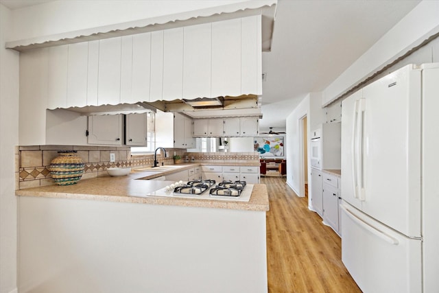 kitchen with a sink, white appliances, a peninsula, light wood finished floors, and light countertops