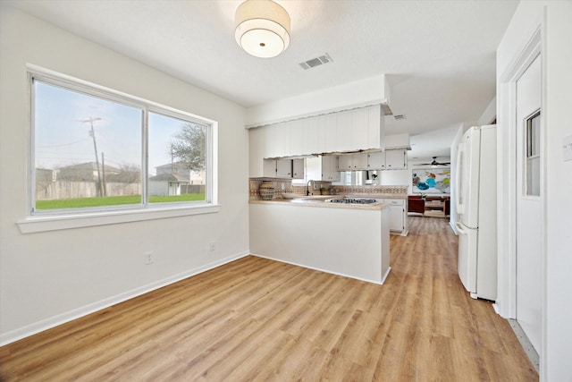 kitchen featuring visible vents, light wood-style flooring, a sink, freestanding refrigerator, and a peninsula