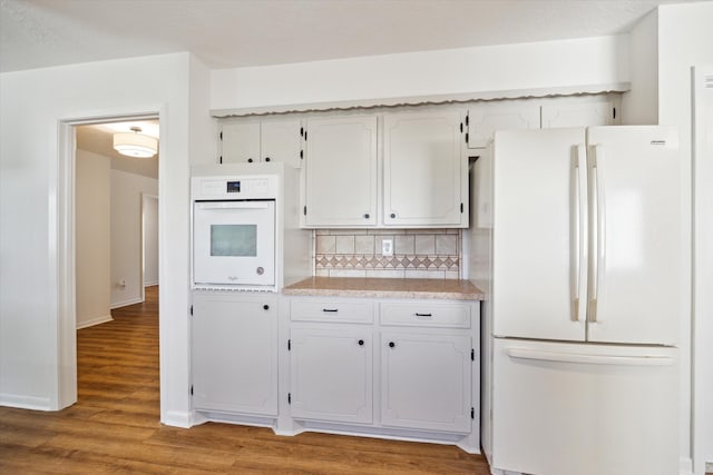 kitchen featuring light wood-type flooring, decorative backsplash, white appliances, and light countertops