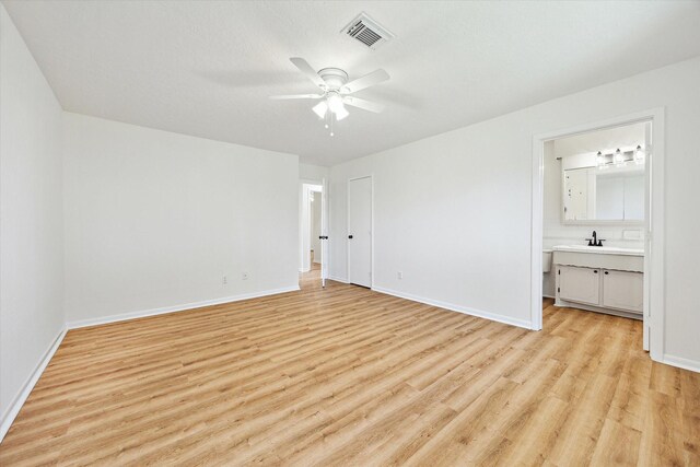 unfurnished bedroom featuring visible vents, baseboards, a sink, light wood-style floors, and ensuite bathroom