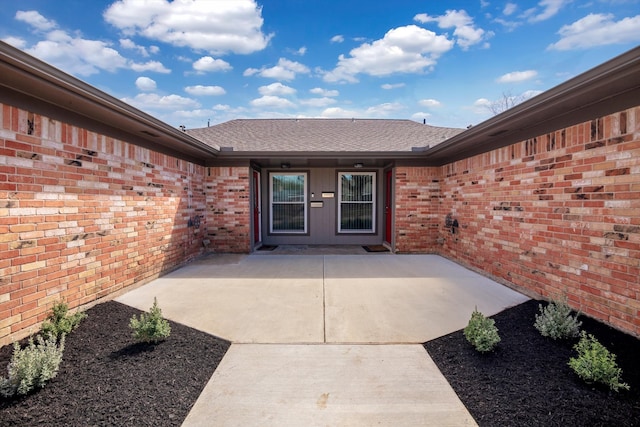 entrance to property with a patio area, a shingled roof, and brick siding