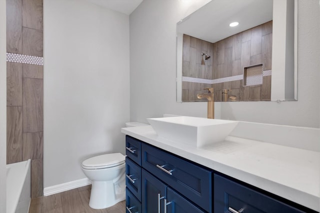 full bath featuring baseboards, toilet, a tile shower, wood finished floors, and vanity