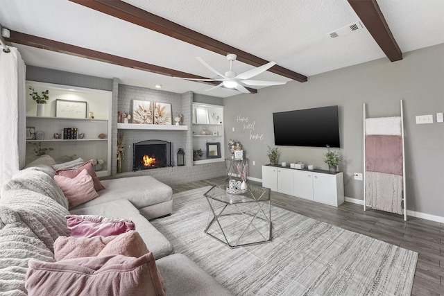 living room featuring a ceiling fan, visible vents, baseboards, a fireplace, and beamed ceiling