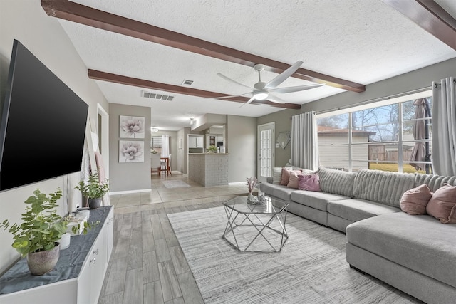 living room featuring ceiling fan, beamed ceiling, a textured ceiling, and light wood-style flooring