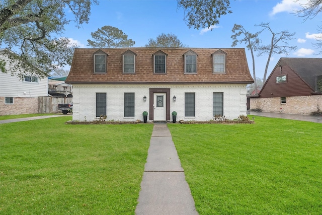 view of front of property featuring brick siding, mansard roof, a front lawn, and roof with shingles