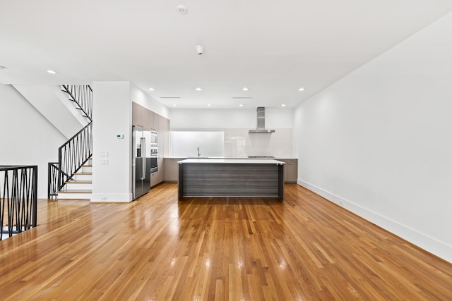 kitchen featuring modern cabinets, wall chimney range hood, light wood-style floors, appliances with stainless steel finishes, and light countertops