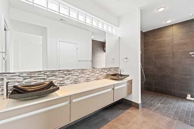 full bathroom with decorative backsplash, tile patterned flooring, vanity, and a tile shower