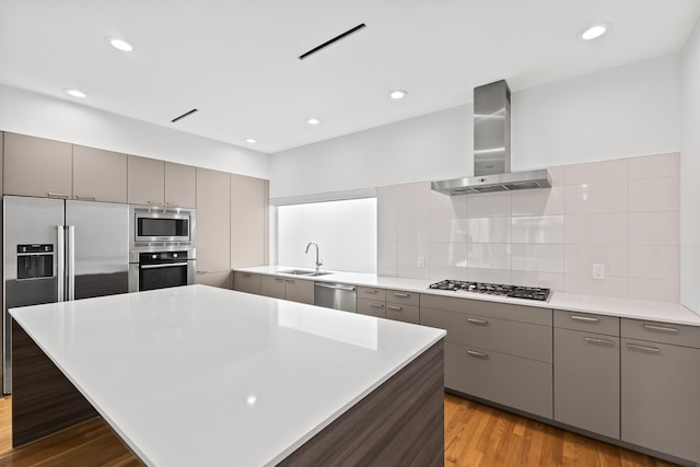 kitchen featuring light wood-type flooring, gray cabinets, stainless steel appliances, wall chimney range hood, and decorative backsplash